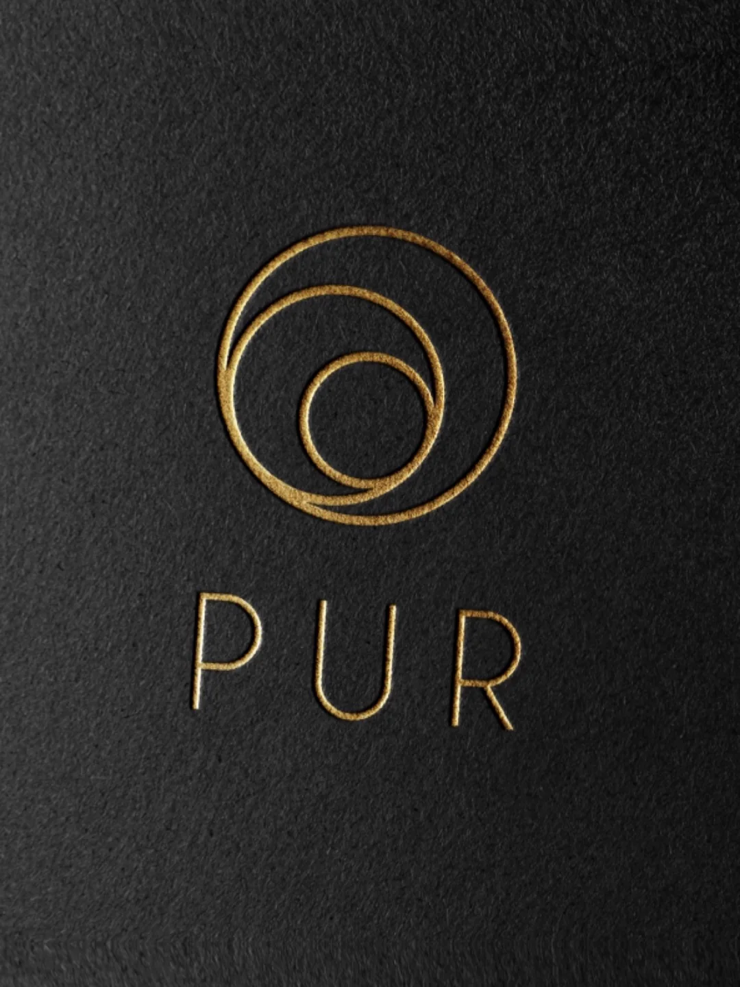 Goldenes PUR-Logo mit drei Ringen, geprägt auf schwarzem Karton
