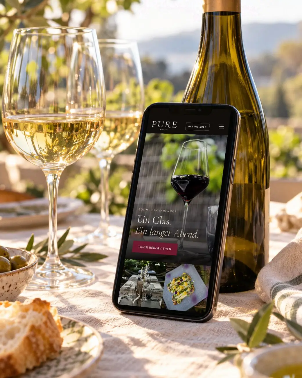 Smartphone mit der Website von PURE wine & food im Garten des Restaurants